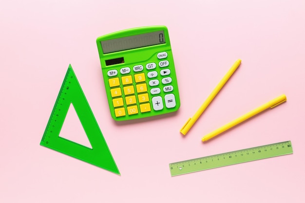 Calculator pens and rulers on a pink background A set of school supplies Flat lay