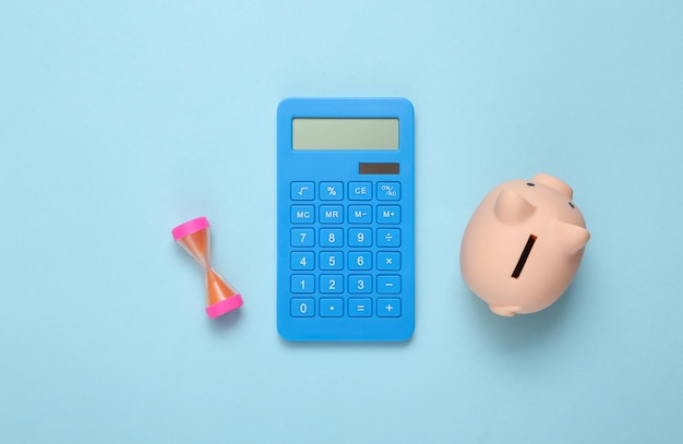 青い背景の電卓貯金箱と砂時計収入計算投資預金