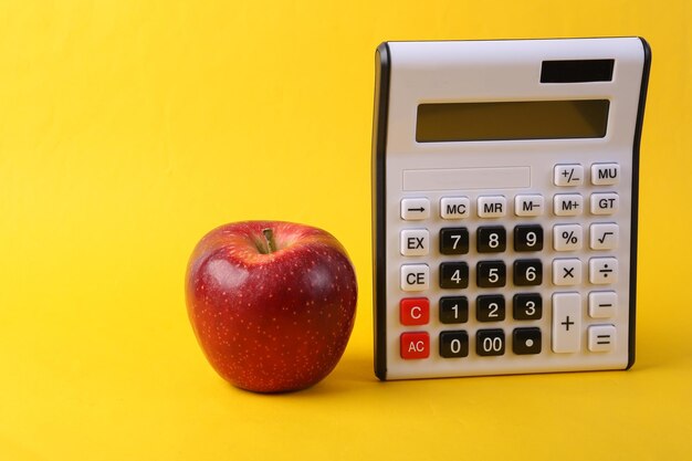 Calculator and red apple on yellow background