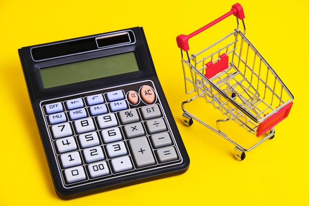 Calculator and shopping cart on yellow backgroundconcept of shopping and grocery shopping