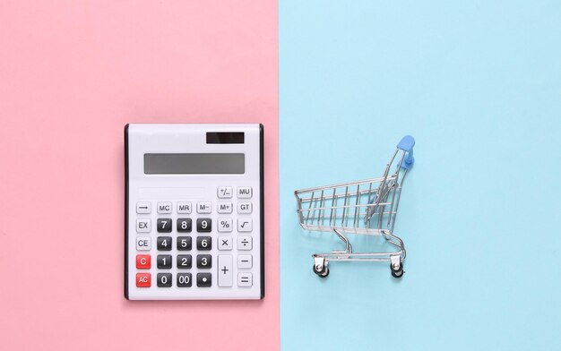 Calculator and shopping trolley on a bluepink pastel background Top view