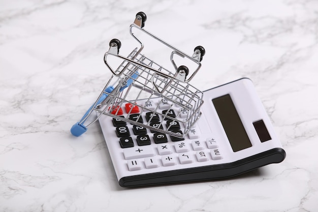 Calculator and shopping trolley on white marble background