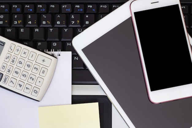 Calculator, smartphone and tablet on the laptop keyboard, business concept