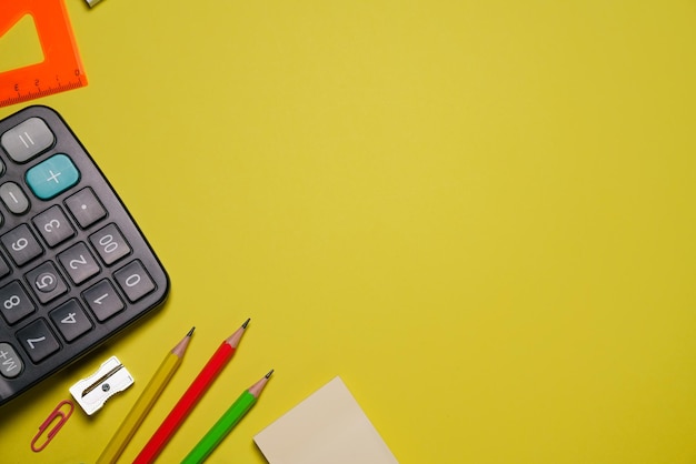 Calculator and stationery in different colors on a yellow background with copy