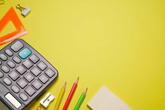 Calculator and stationery in different colors on a yellow background with copy