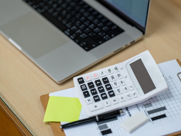 Calculator with laptop computer and document report placed on\
wood desk in officebusiness finances and accounting concept