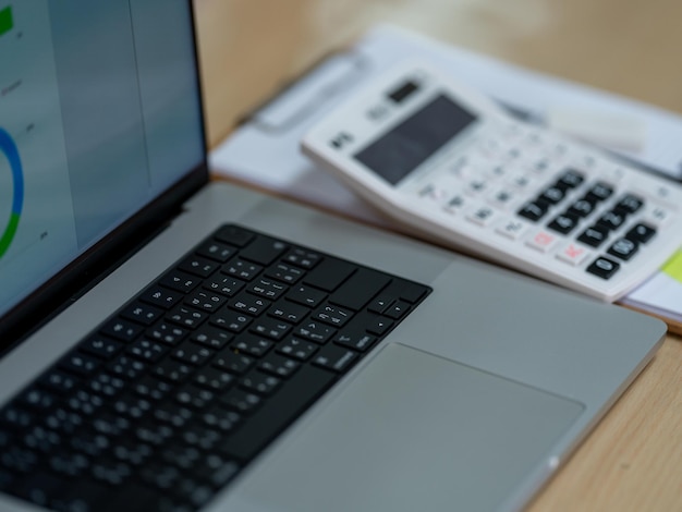 Calculator with laptop computer and document report placed on\
wood desk in officebusiness finances and accounting concept