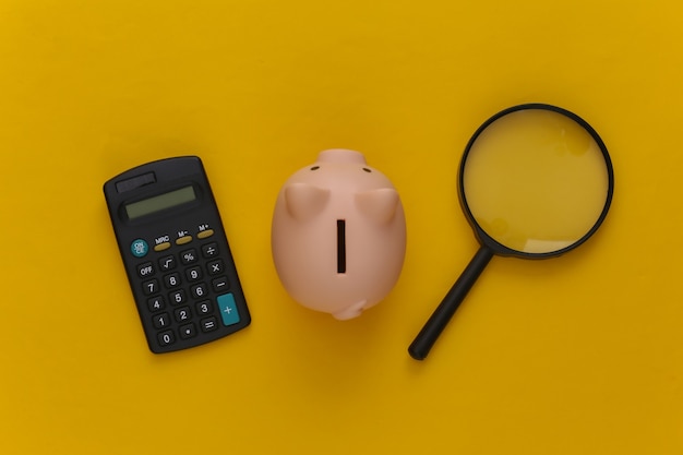 Calculator with magnifier and piggy bank on yellow