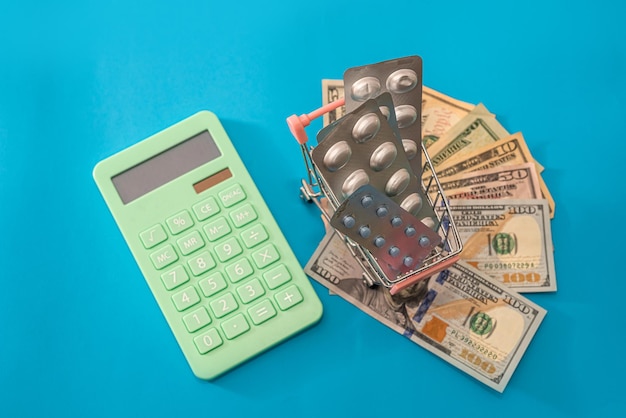 Калькулятор с новыми долларами на тележке, в которой таблетки лежат на синем фоне. Концепция покупок.