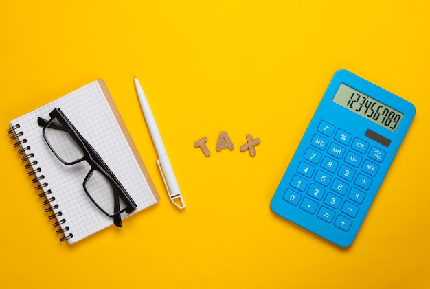 Calculator with the word tax and notebook with glasses on yellow.