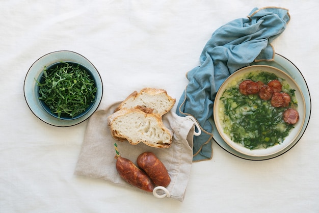 Caldo Verde Soep met groenten en gehakte chorizo bovenop in een keramische kom boven een servet. Bovenaanzicht