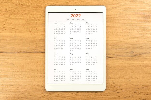 Calendar 2022 on the screen. wooden table background, business\
desktop, to do goals and planning for new year concept. top view\
photo