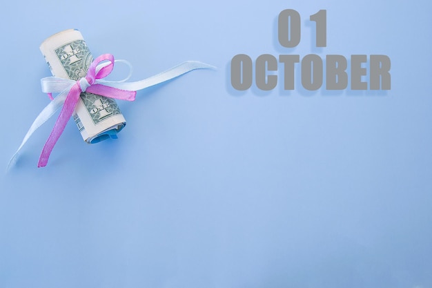 Calendar date on blue background with rolled up dollar bills pinned by blue and pink ribbon with copy space October 1 is the first day of the month