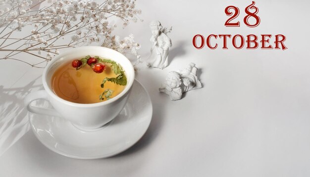 Календарная дата на светлом фоне с фарфоровой чашкой зеленого чая, белой гипсофилой и ангелами с копией пространства 28 октября - двадцать восьмой день месяца