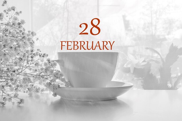 磁器の白いお茶のペアと白いカスミソウと明るい背景のカレンダーの日付2月28日