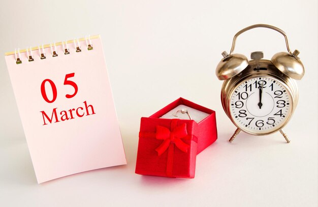 반지와 알람 시계가 있는 빨간색 선물 상자가 있는 밝은 배경의 달력 날짜 3월 5일