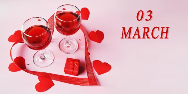 Foto data del calendario su sfondo chiaro con due bicchieri di vino rosso confezione regalo rossa e cuori rossi 3 marzo