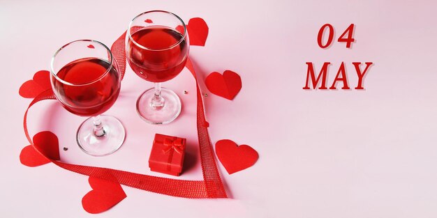 Calendar date on light background with two glasses of red wine red gift box and red hearts may 4