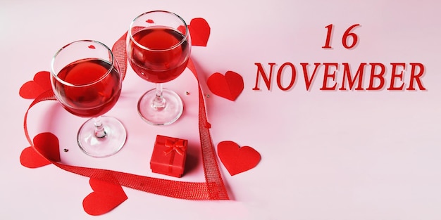 Calendar date on light background with two glasses red wine red gift box and red hearts november 16