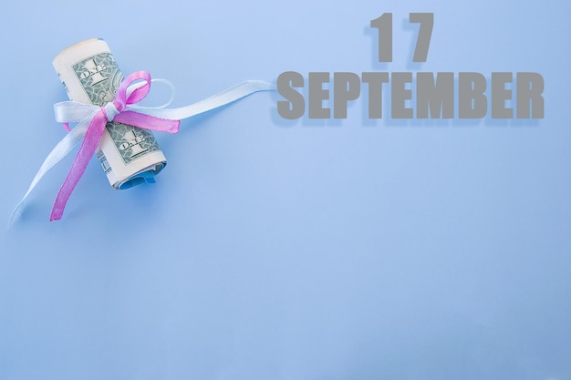 Фото Календарная дата на синем фоне со свернутыми долларовыми купюрами, закрепленными сине-розовой лентой с копией пространства 17 сентября - семнадцатый день месяца