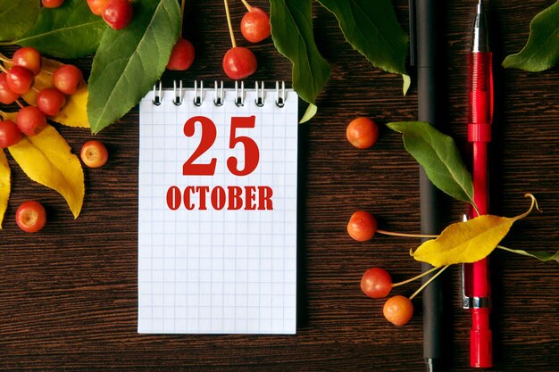 Фото Календарная дата на деревянном темном фоне рабочего стола с осенними листьями и маленькими яблоками 25 октября — двадцать пятый день месяца