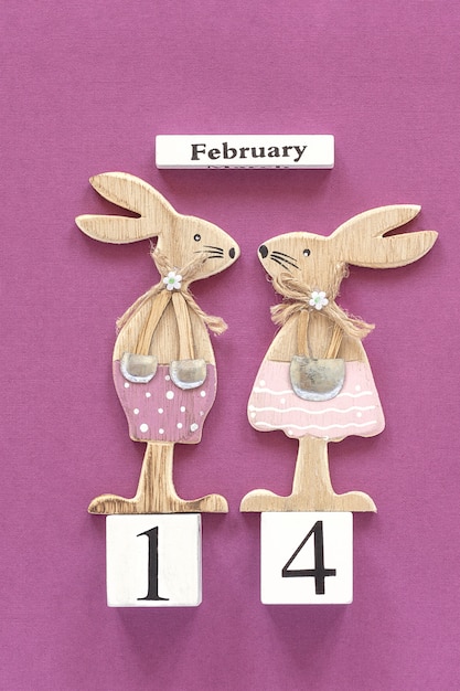 Photo calendar february 14th and pair of wooden lovers rabbits on purple background.