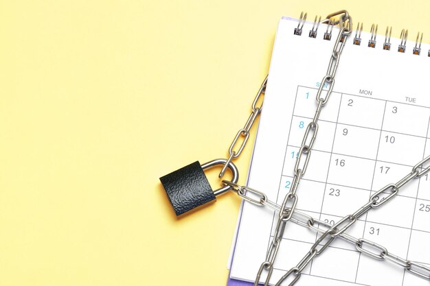 Calendar is wrapped in a chain and closed with a padlock Yellow background Template Copy space for text mockup