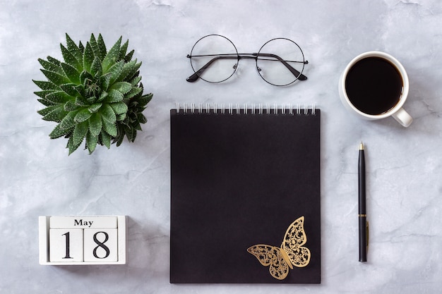  calendar May 18. Black notepad, cup of coffee, succulent, glasses on marble 