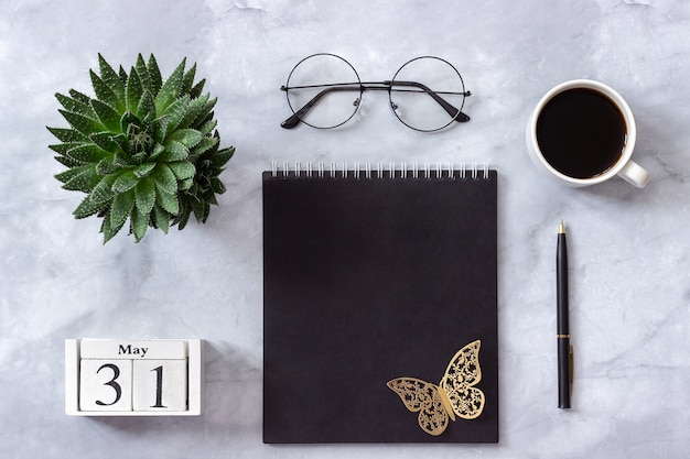  calendar May 31. Black notepad, cup of coffee, succulent, glasses on marble