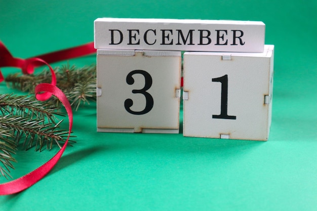 Photo calendar numbers 3 and 1 on cubes with spruce branches red ribbon on a green background side view closeup