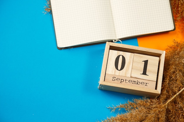 사진 숫자와 달이 있는 나무 큐브 달력입니다. 흰색 시트가 있는 메모장. 학년도의 첫날. 나무 달력에서 숫자를 선택합니다. 9월 1일. 9월 날짜