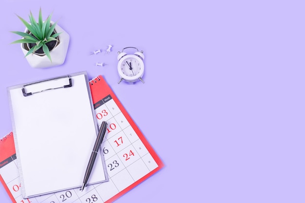 Calendar open notebook pen with alarm and green flowerpot on\
purple background business education working concept