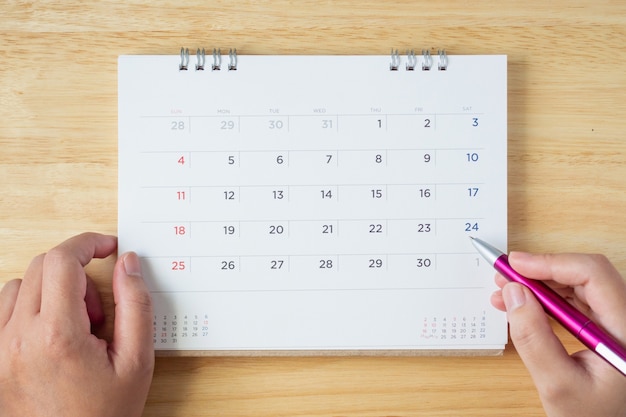 Calendar page on table with female hand holding pen