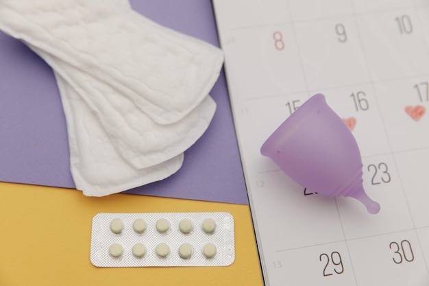 Photo calendar, sanitary pads and menstrual cup with pain relief pills close-up. woman critical days and hygiene protection.