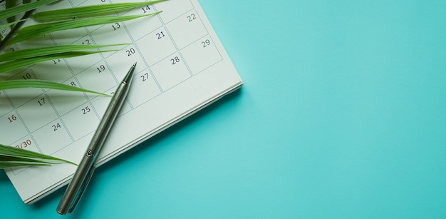 calendar with pen and tropical leaves on blue background for holiday summer