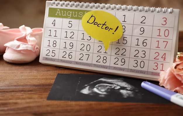 Calendar with ultrasound scan of baby on wooden background