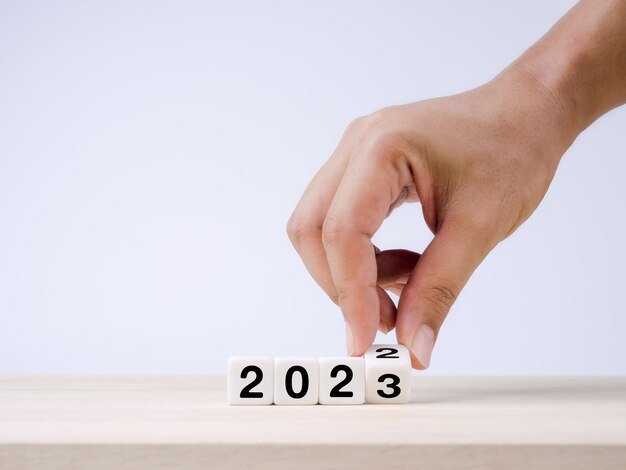 暦年 2022 年は 2023 年の成功の概念に変更されました 2022 年から 2023 年に移行するために手で回転する白い立方体のブロックは、メリー クリスマスと新年あけましておめでとうございます青の背景に準備します