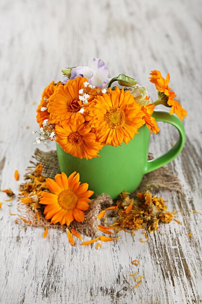 Photo calendula flowers in cup on wooden background