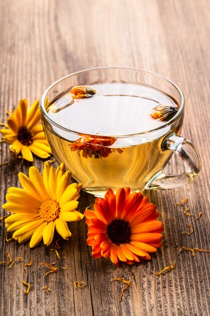 Calendula (Marigold) herbal tea in a transparent glass mug with dried flowers on wooden rural background.