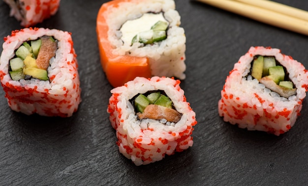 Калифорнийские суши с красной икрой тобико и кусочками суши филадельфия на черной грифельной доске