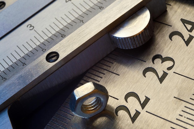 Caliper and nuts with a bolt a metalwork measuring tool lies on the background of metal rulers closeup