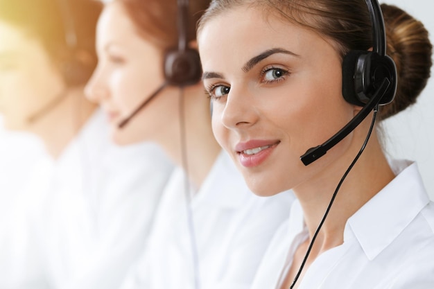 Call center. Beautiful young woman using headset and computer to help customers in sunny office. Business concept.
