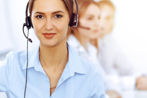 Call center operators. Focus on beautiful business woman using headset in sunny office.