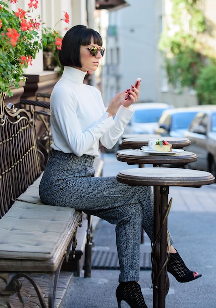 Call friend Leisure concept Girl fashionable lady with smartphone Pleasant time and leisure Relax and coffee break Woman attractive elegant brunette spend leisure cafe terrace background