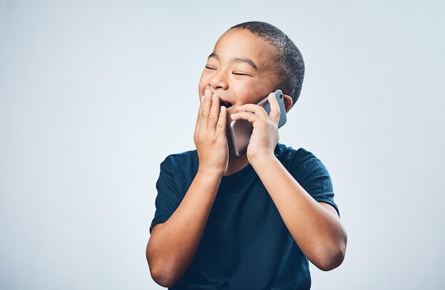 A call from grandma always gives him the giggles Studio shot of a cute little boy looking amazed while using a smartphone against a grey background