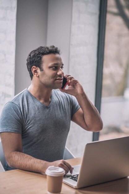 On the call. Young businessman sitting at the table in the office and talking on the phone