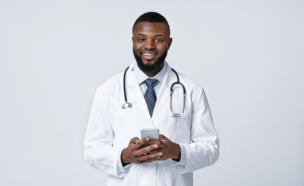 call your doctor during isolation happy african doctor holding mobile phone over white studio