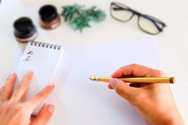 Photo calligraphy expert holding fountain pen over paper on table