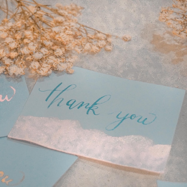 Calligraphy thank you card and dried flowers on white wooden background Vintage toned