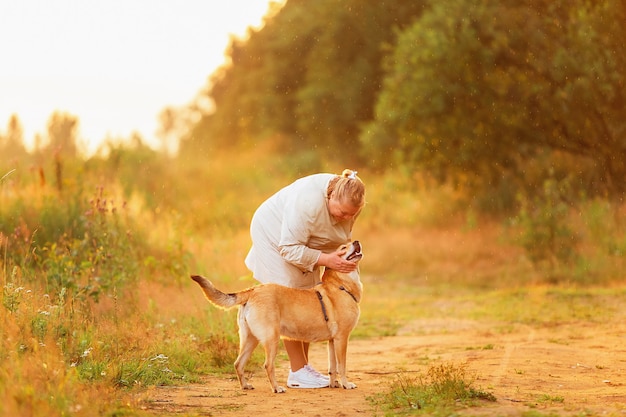 Calm aged lady with hands behind back and glad mixed breed dogs walking in countryside